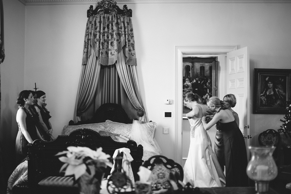 A bride is helped into her dress by her mother and maid of honor at the Fountainview mansion, photographed by Detroit Wedding Photographer Heather Jowett.