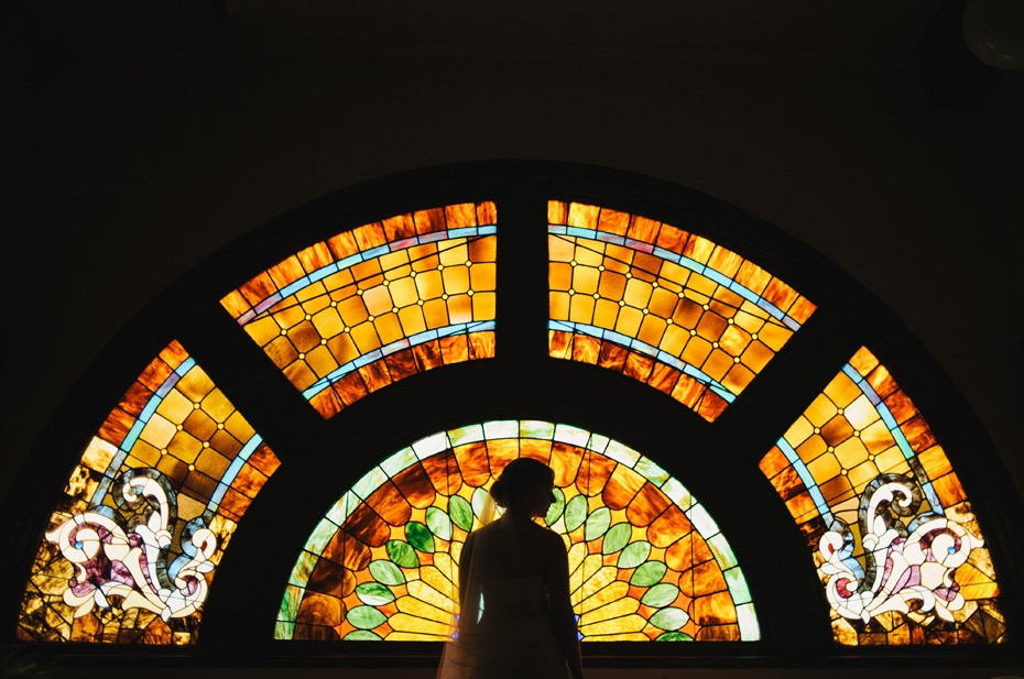 A bride stands in front of stained glass windows at a church.