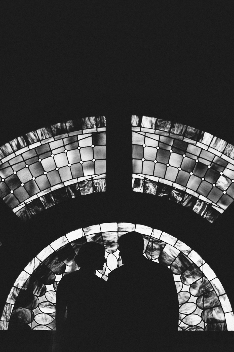 A silhouette of a bride and groom against stained glass windows, photographed by Ann Arbor Wedding Photographer Heather Jowett.