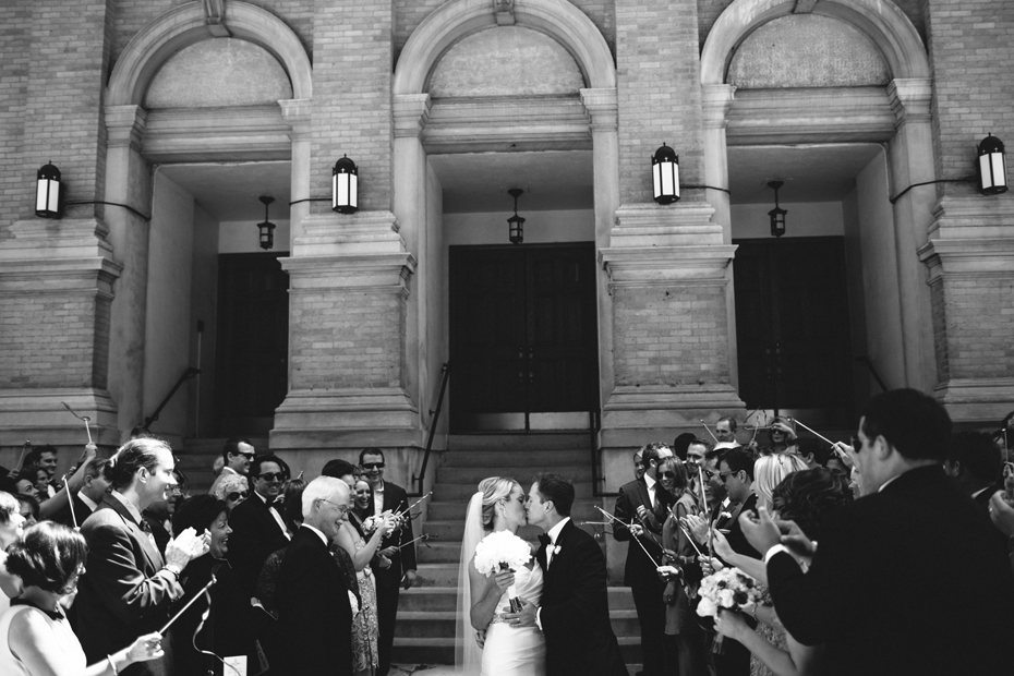 Bride and groom exit the church while their guests wave streamers, photographed by Michigan Wedding Photographer, Heather Jowett.