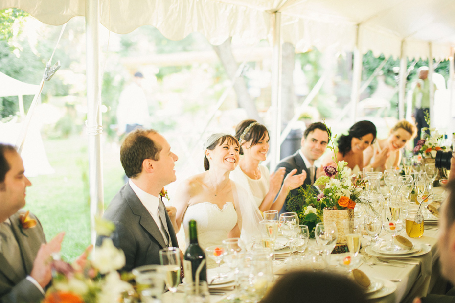 The bride and groom laugh during toasts at their rustic vintage style backyard wedding in Bloomfield Hills, photographed by Michigan wedding photographer, Heather Jowett.