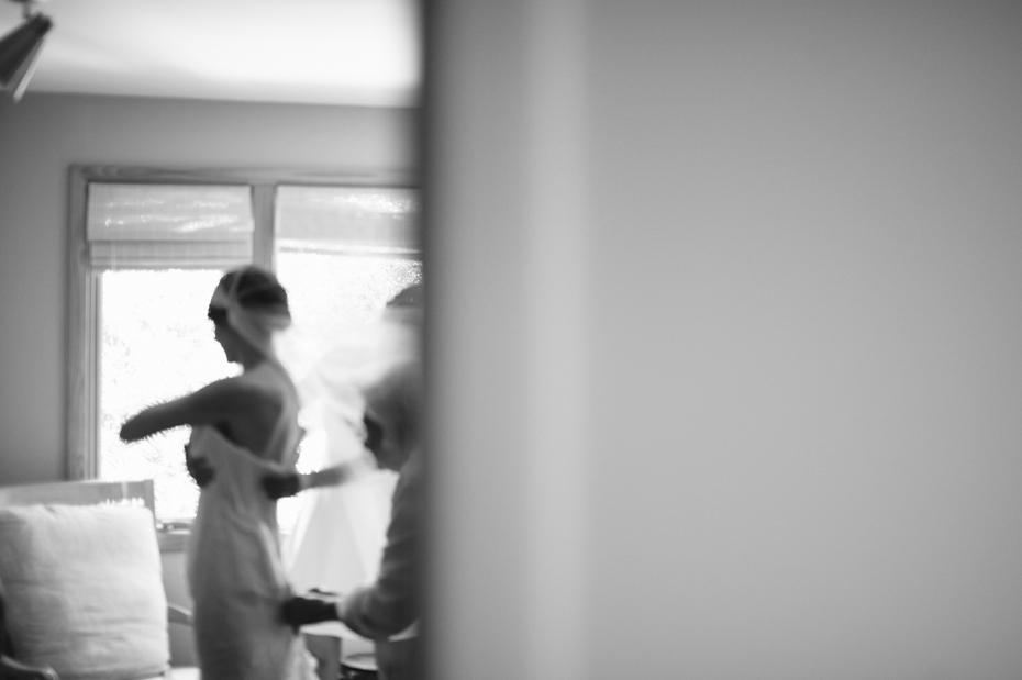 A bride puts on her wedding dress in this black and white photograph by Ann Arbor Michigan wedding photographer, Heather Jowett.