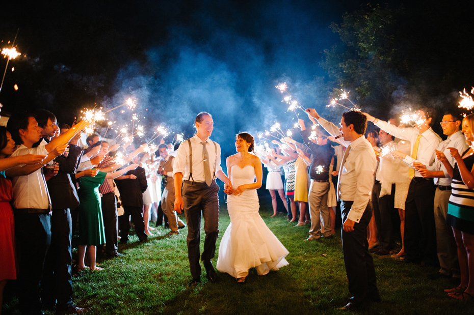 The bride and groom exit their wedding reception while guests hold sparklers at a backyard wedding by Bloomfield Hills wedding photographer Heather Jowett.