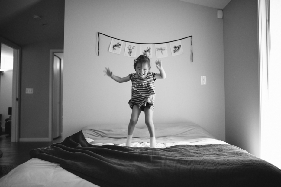 A 2 year old jumps on the bed during a documentary family portrait session in Ferndale photographed by Ann Arbor Wedding Photographer, Heather Jowett.