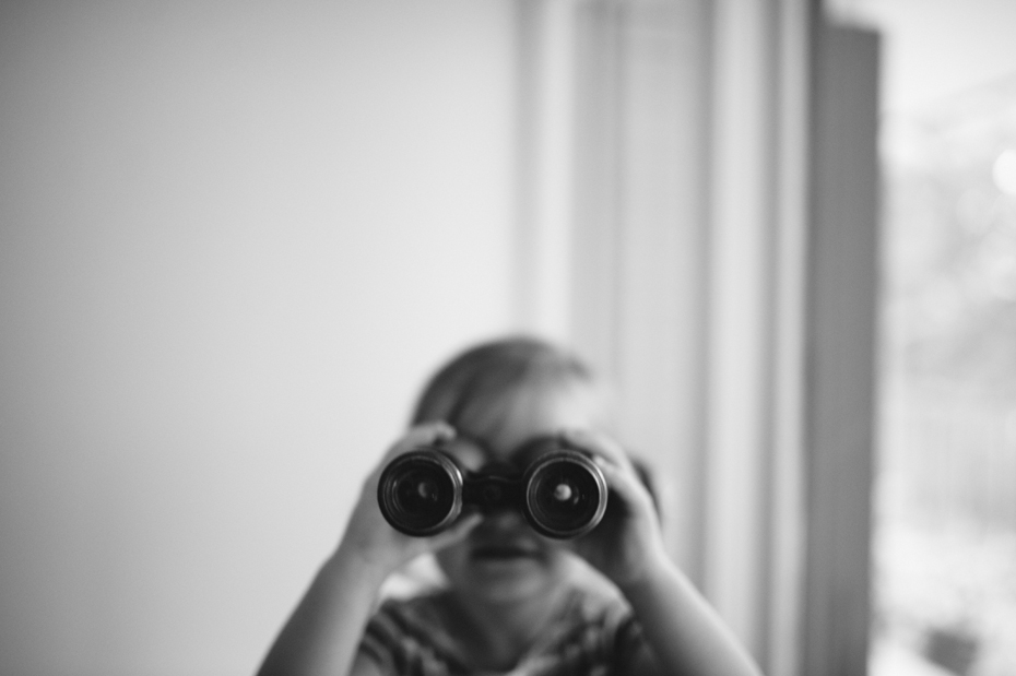 A two year old plays with binoculars during a documentary family portrait session in Ferndale photographed by Ann Arbor Wedding Photographer, Heather Jowett.