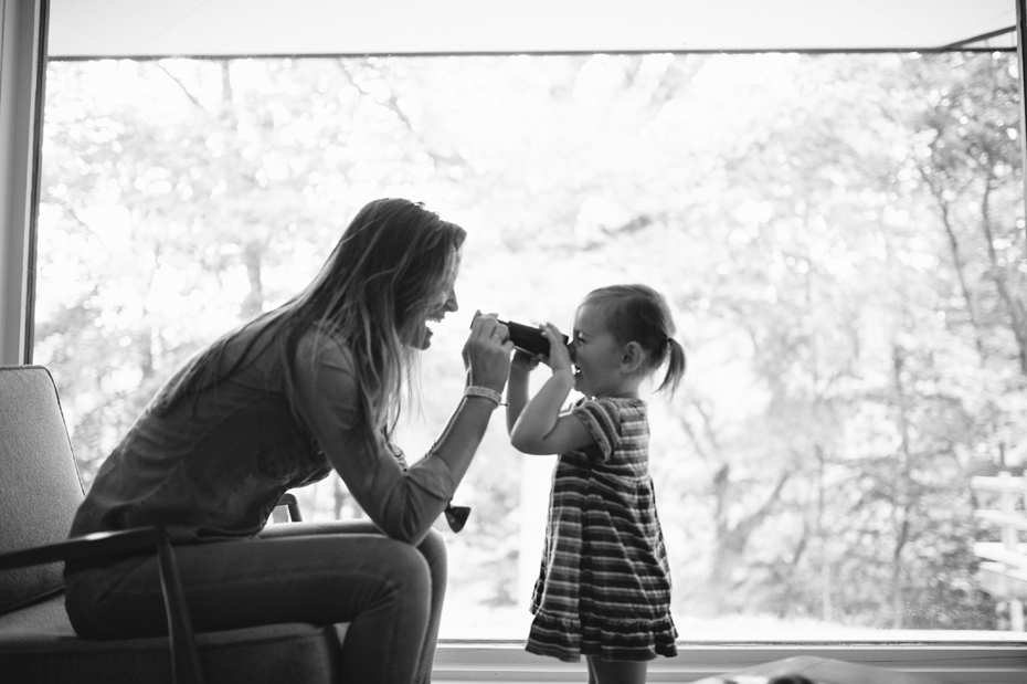 A two year old and her mother play with binoculars during a documentary family portrait session in Ferndale photographed by Ann Arbor Wedding Photographer, Heather Jowett.