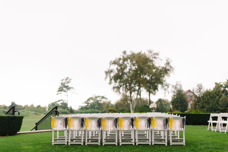 Yellow and grey streamers decorate chairs for a wedding ceremony held outside at The Inn at Stonecliffe on Mackinac Island by Michigan Wedding Photographer Heather Jowett.