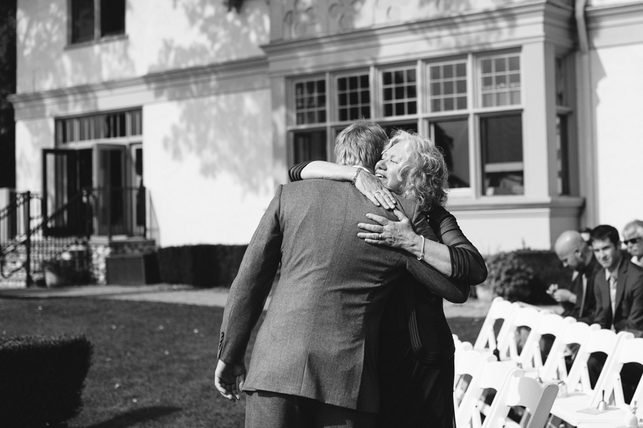 A groom hugging his mother before the start of a wedding ceremony held outside at The Inn at Stonecliffe on Mackinac Island by Detroit Wedding Photographer Heather Jowett.