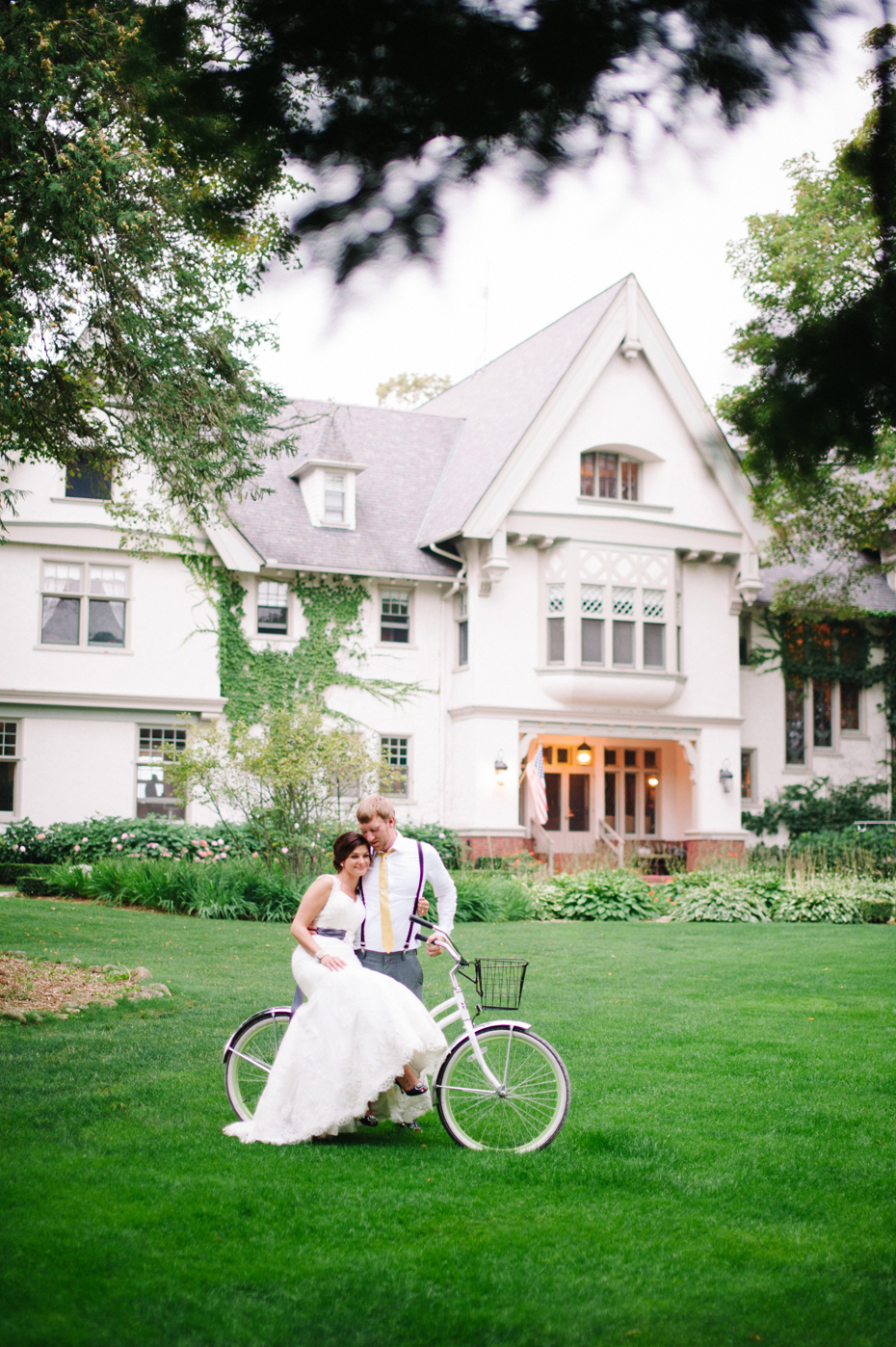 Bride and groom pose with bicycles on the front lawn during an outdoor wedding reception at The Inn at Stonecliffe on Mackinac Island by Ann Arbor Wedding Photographer Heather Jowett.