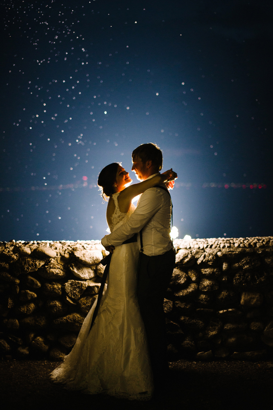 Bride and groom pose at night with the lights of the Mackinac bridge in the background during an outdoor wedding reception at The Inn at Stonecliffe on Mackinac Island by Ann Arbor Wedding Photographer Heather Jowett.