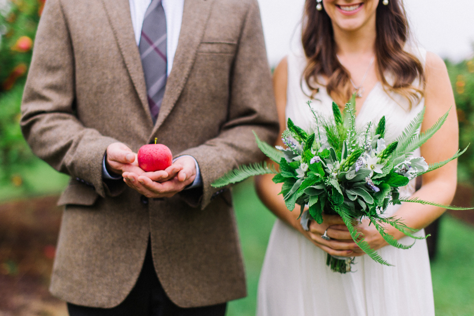 Bride holds her herb bouquet in a beautiful apple orchard after their elopement by Ann Arbor Michigan Wedding Photographer Heather Jowett.