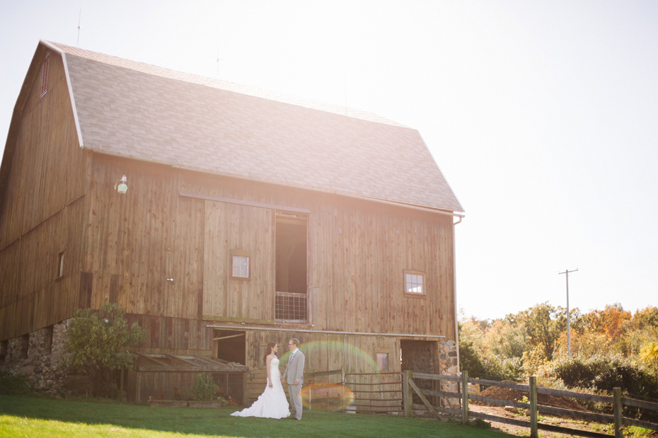 Bride and groom pose by the barn at Misty Farms by photojournalistic Michigan wedding photographer Heather Jowett.