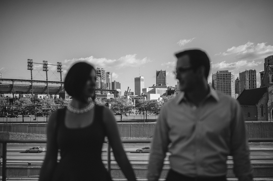 A couple poses for an engagement photo with Comerica Park and the Detroit Skyline in the background.
