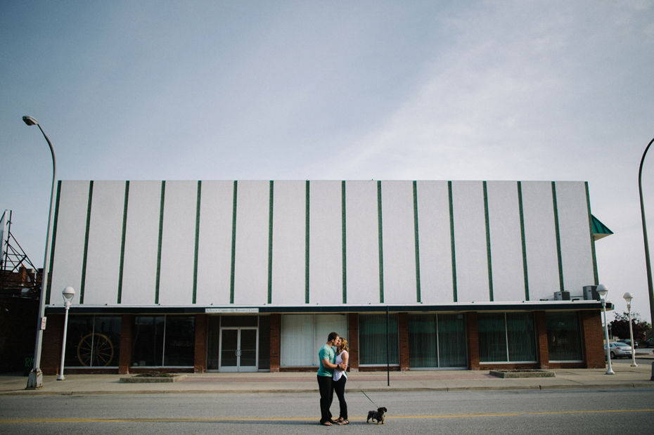 Couple poses in the middle of the street with their dog during their engagement session in Port Huron Michigan.