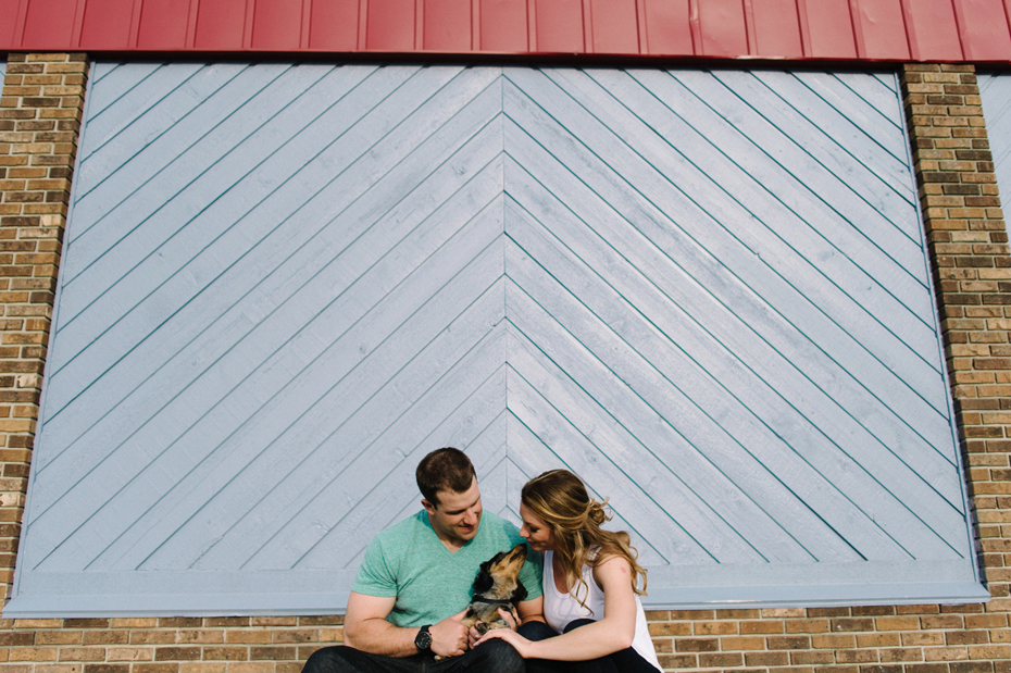 A dappled dachshund dog shares a kiss with his humans during an engagement session.