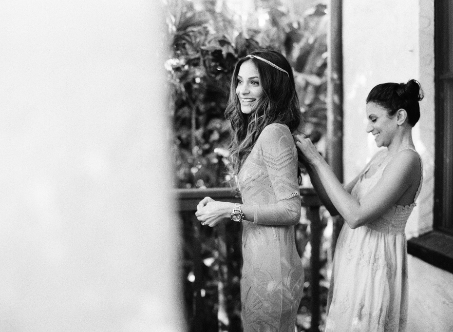 Bride's sister helps her get dressed in her red Roberto Cavalli dress for her wedding at the Sundy house by wedding photographer Heather Jowett.