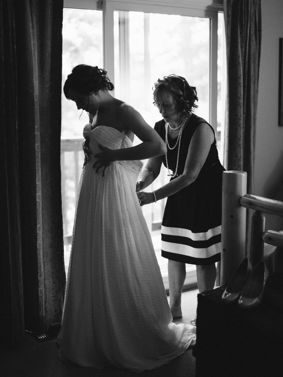 Mother helps her daughter into her Ivy and Aster Sweetpea dress at a rustic cabin wedding in Northern Michigan by wedding photographer Heather Jowett.