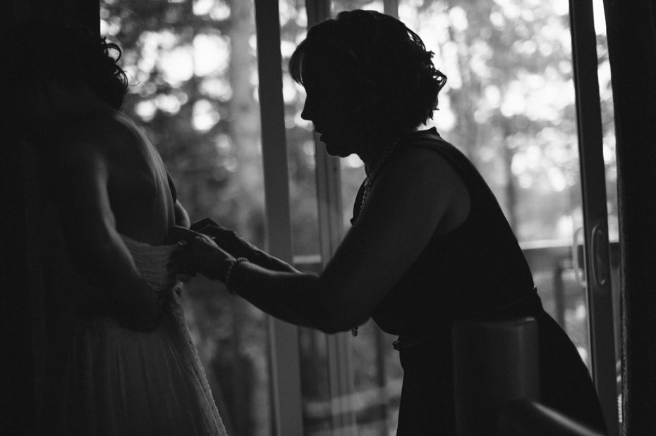 Mother helps her daughter into her Ivy and Aster Sweetpea dress at a rustic cabin wedding in Northern Michigan by wedding photographer Heather Jowett.