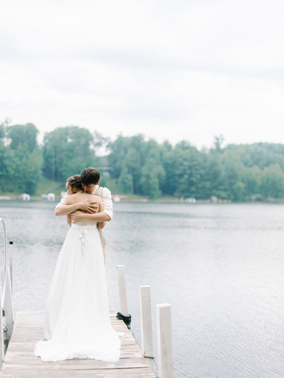 Bride and groom pose for portrait by a lake at a cabin in Northern Michigan.