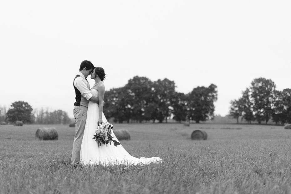 Bride and groom pose for portraits in a hayfield in Northern Michigan by Ann Arbor Wedding Photographer Heather Jowett.