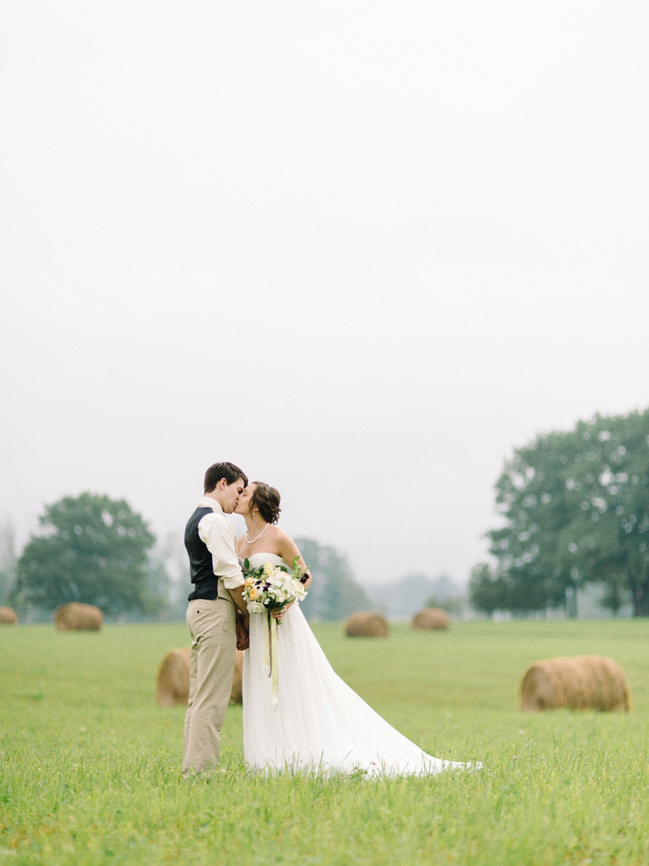 Bride and groom pose for portraits in a hayfield in Northern Michigan by Ann Arbor Wedding Photographer Heather Jowett.