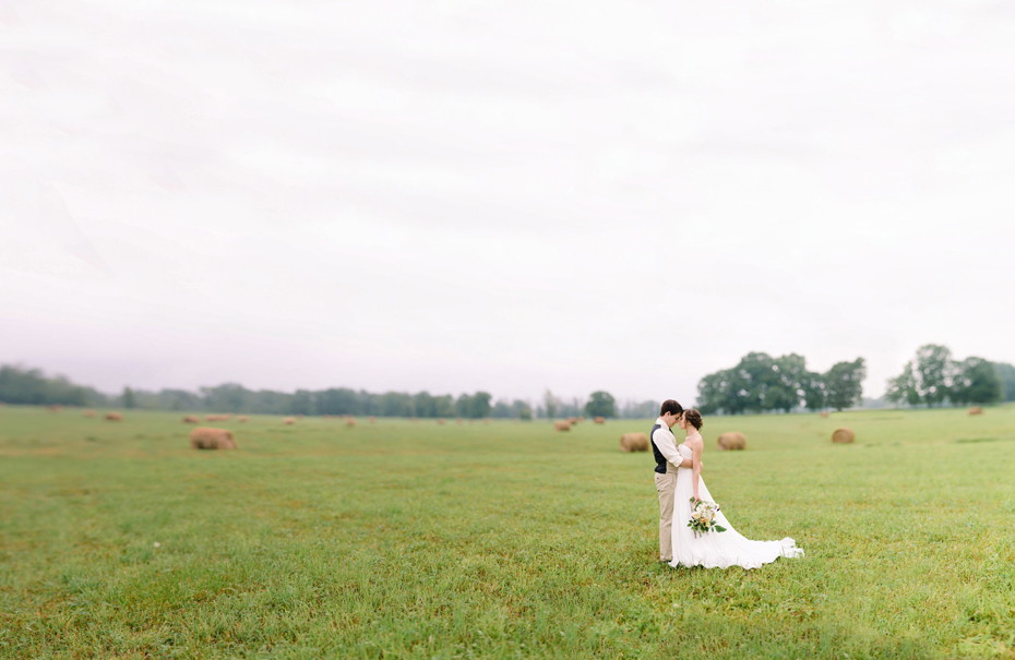 Bride and groom pose for portraits in a hayfield in Northern Michigan by Ann Arbor Wedding Photographer Heather Jowett.