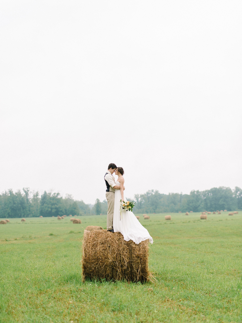 Bride and groom pose for portraits on a hay bale in Northern Michigan by Ann Arbor Wedding Photographer Heather Jowett.