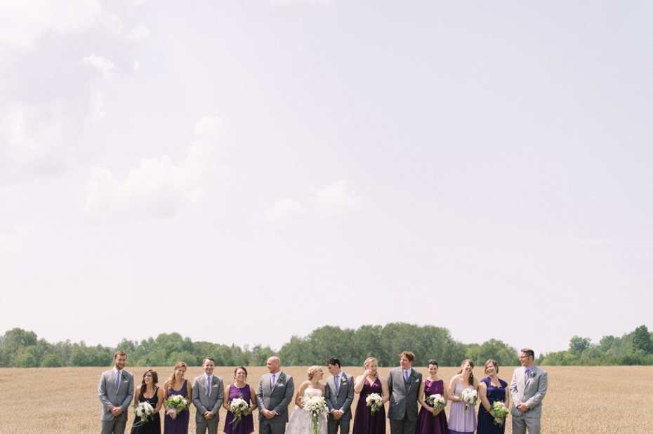 Bridal party wearing different shades of purple by a wheat field by Michigan wedding photographer Heather Jowett.
