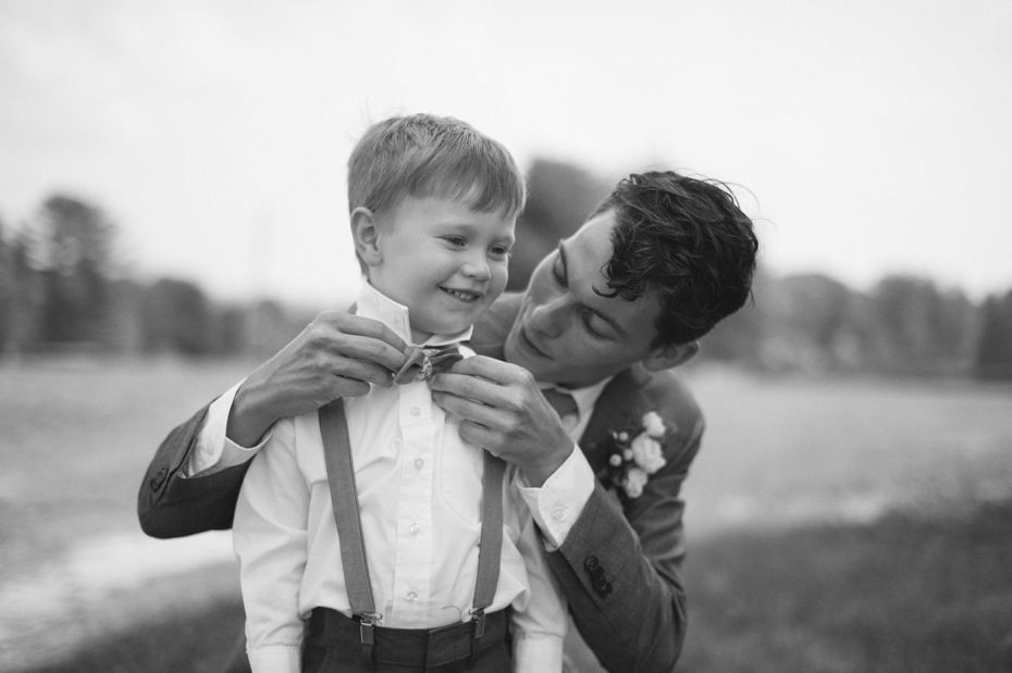 Groom helps the ring bearer into his bow tie by Michigan wedding photographer Heather Jowett.