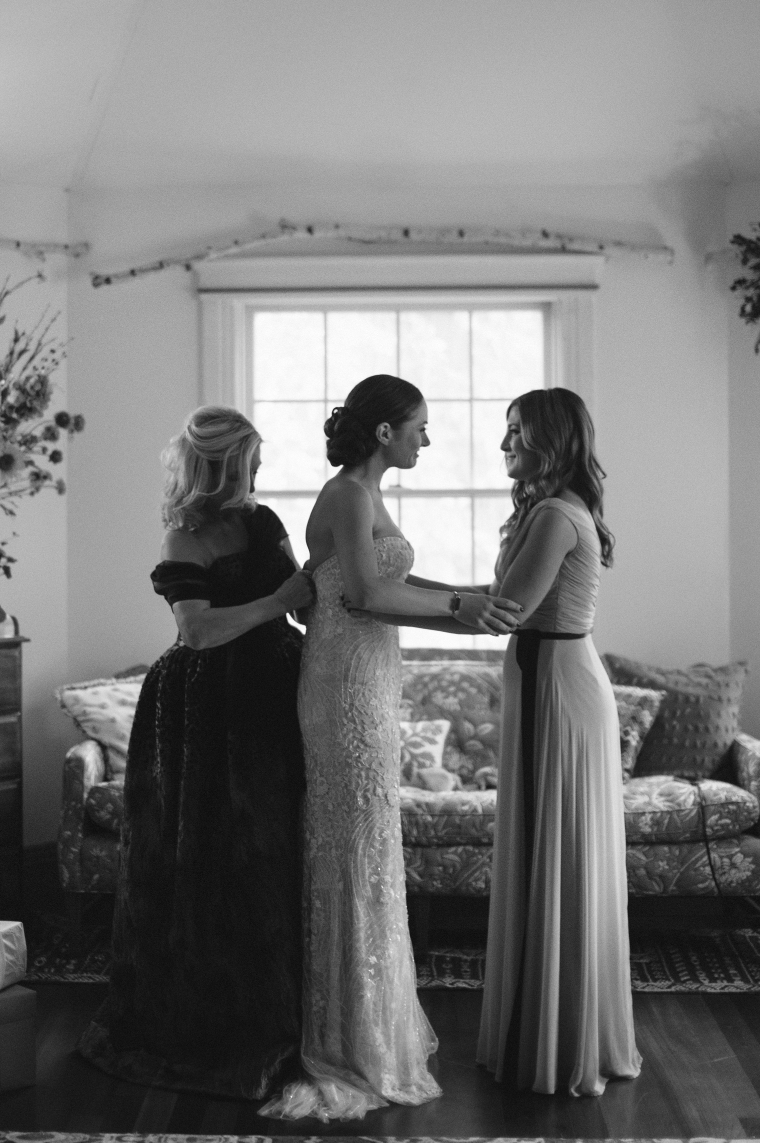 The mother of the bride and maid of honor help a bride into her Monique Lhuillier gown.