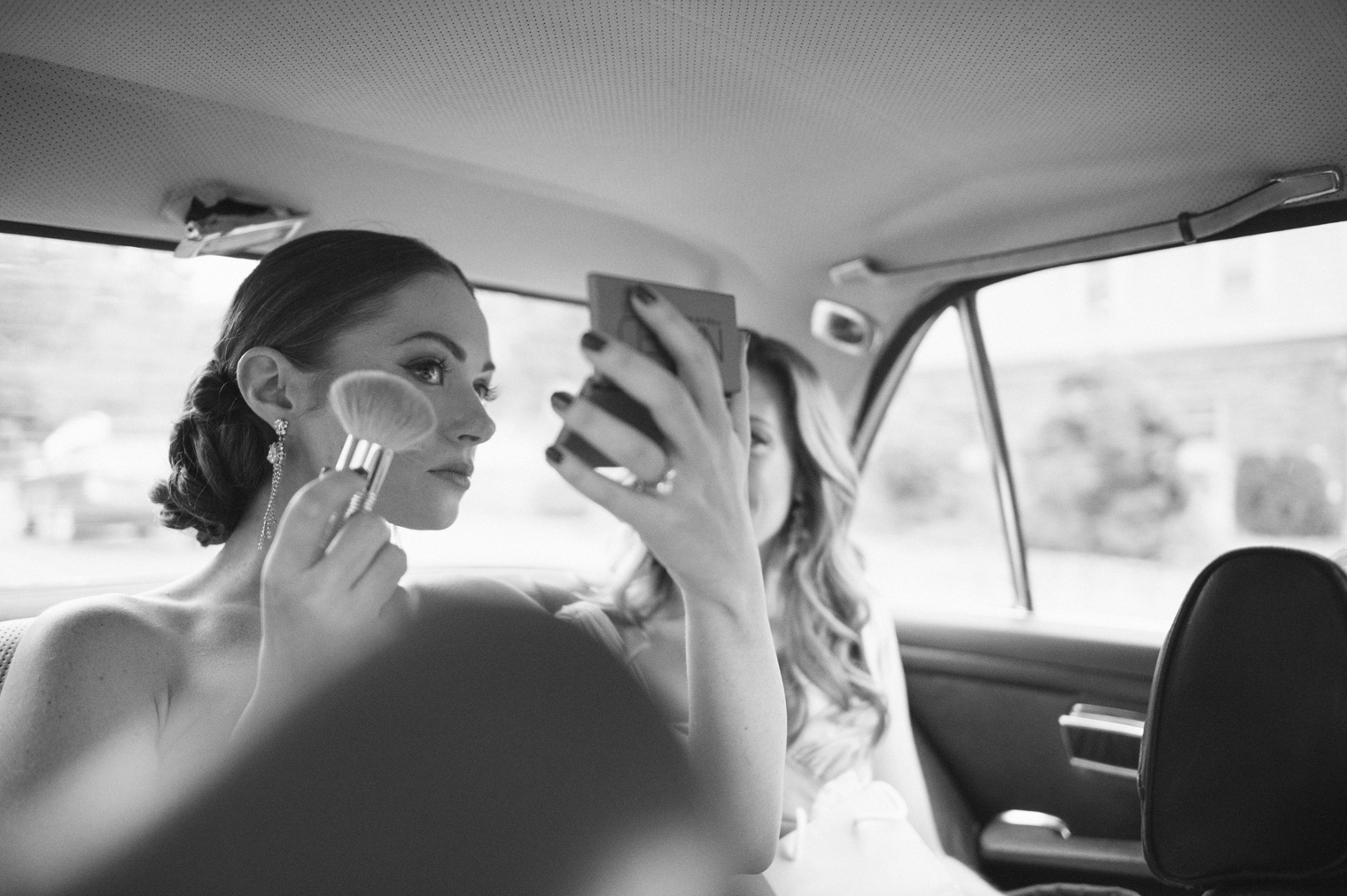 Bride touches up makeup in the back of a classic Mercedes.