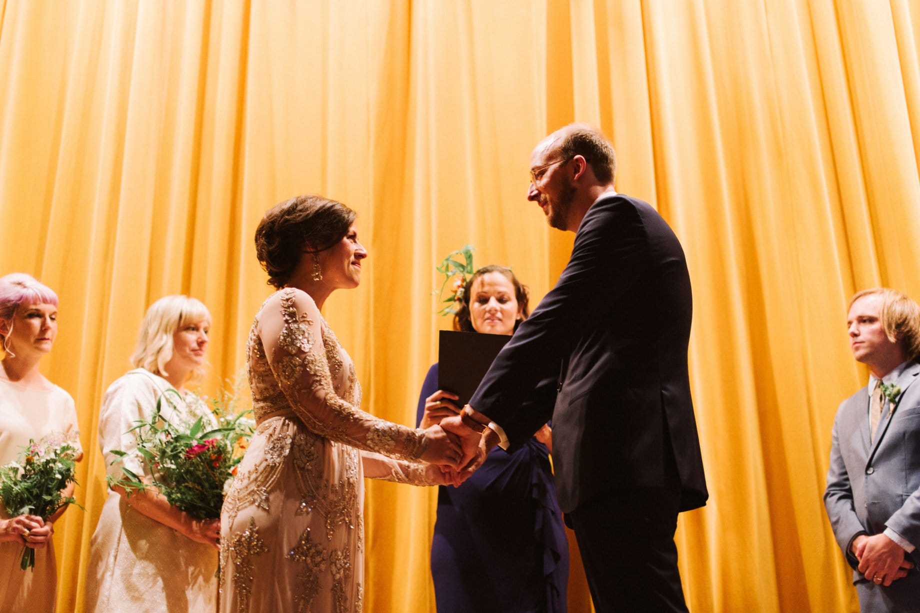 bride and groom exchanging vows in from of golden curtain