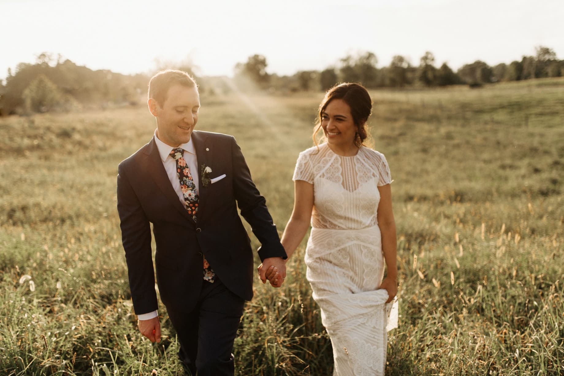 bride and groom walking in field at sunset