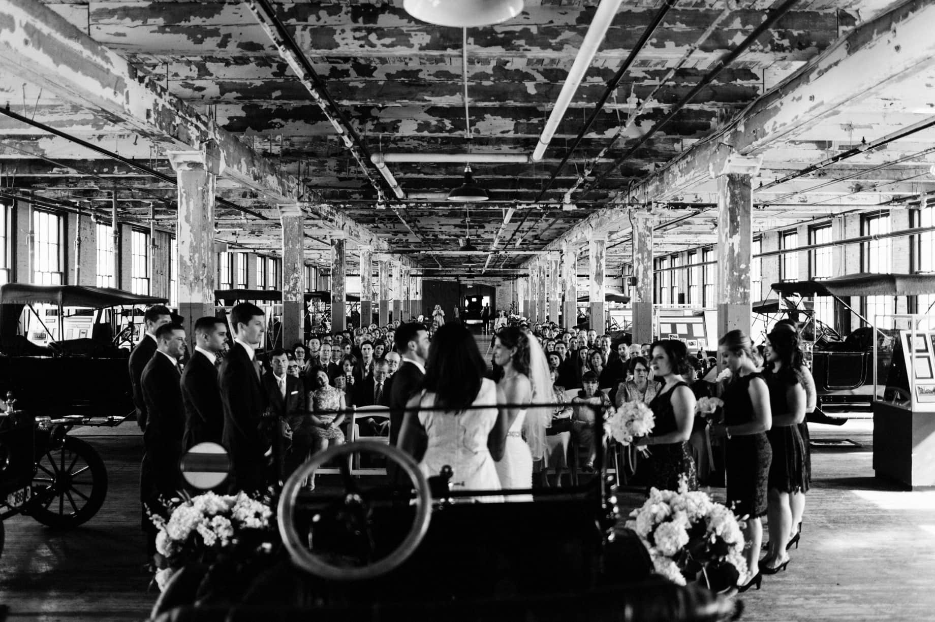 family and friends look on as bride and groom are married at the ford piquette plant in detroit michigan by wedding photographer heather jowett