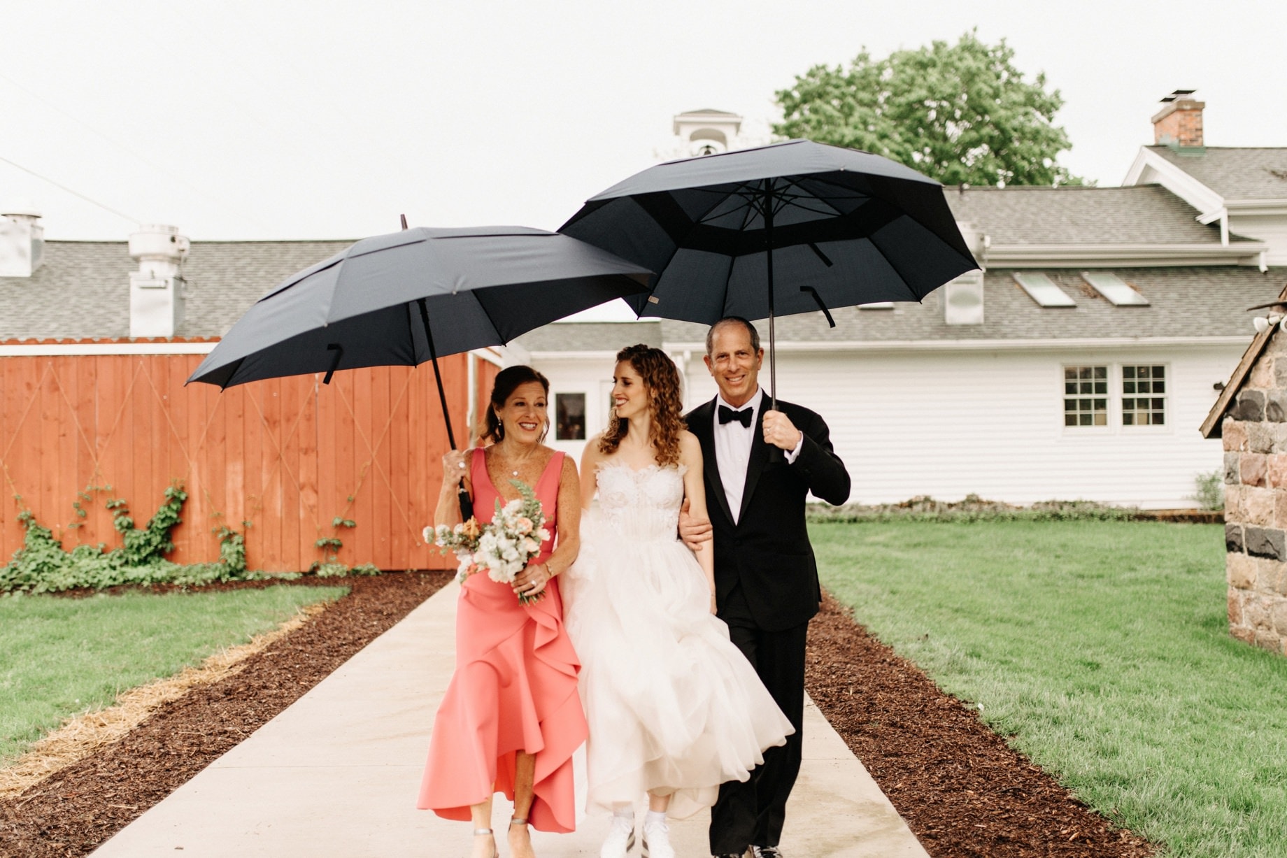 bride walks to the ceremony with her parents in the rain