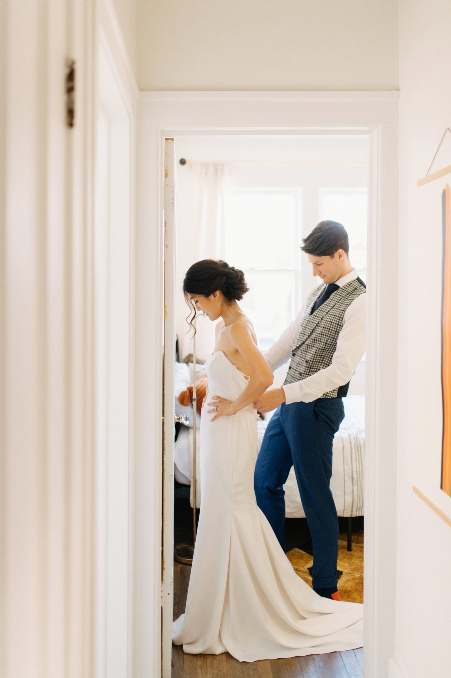 a groom helps his bride into her wedding dress