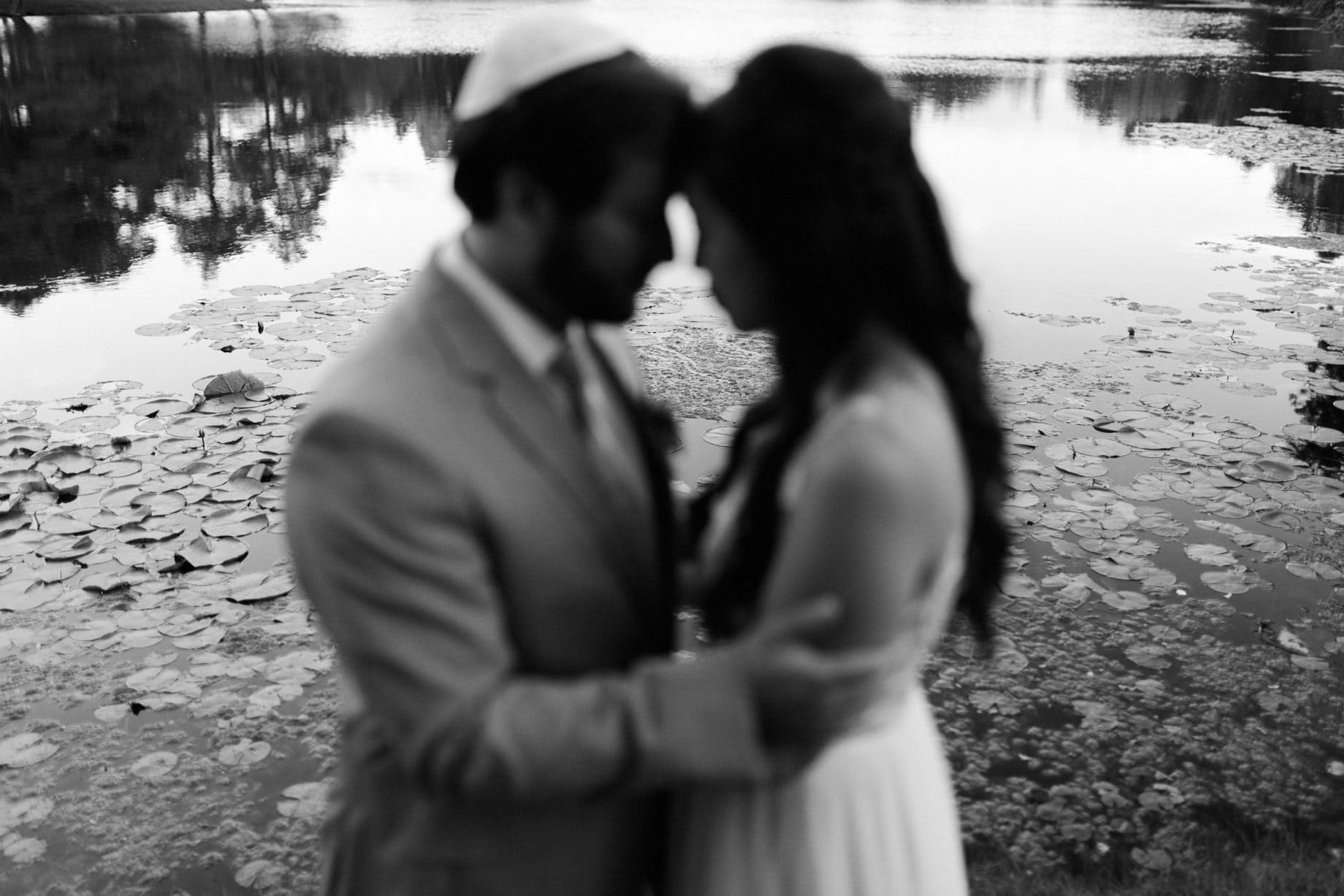 couple poses in front of a pond filled with lily pads