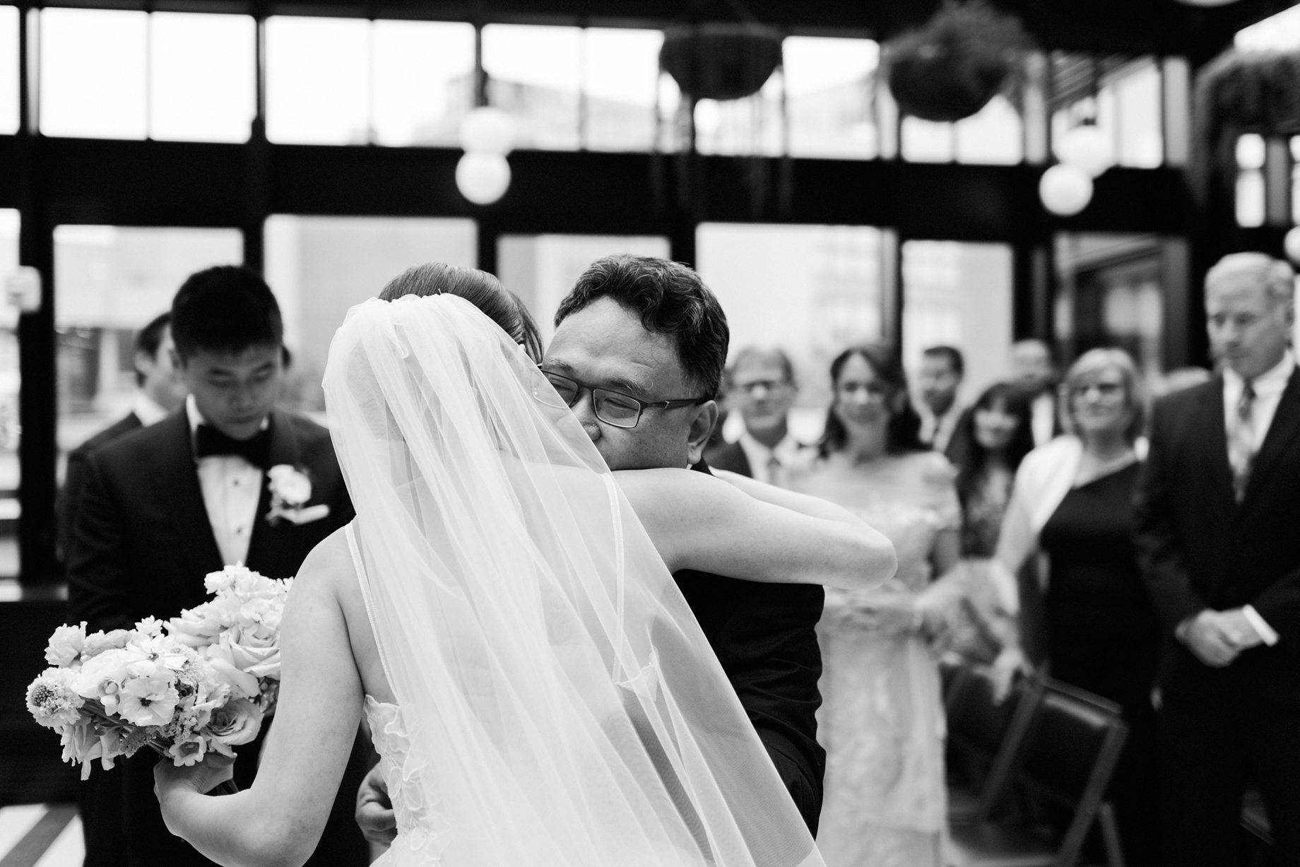 The bride hugs her father at the end of the aisle as the groom watches tenderly in the background