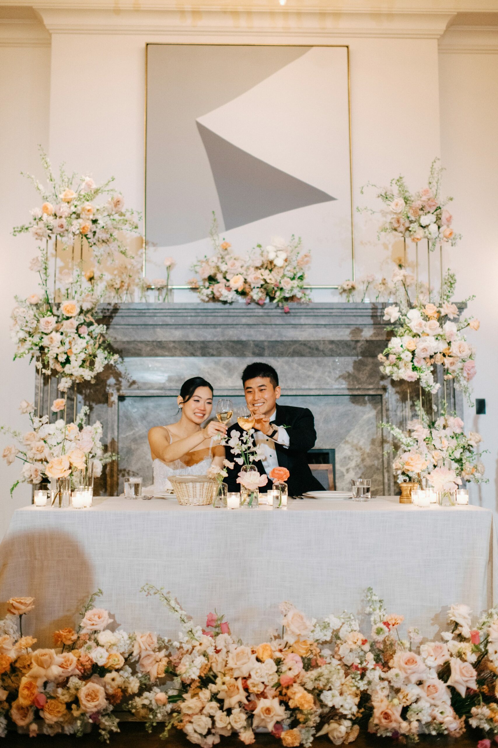 Newlywed couple clink champagne glasses in a celebratory toast at their flower draped sweetheart table during their Detroit wedding reception