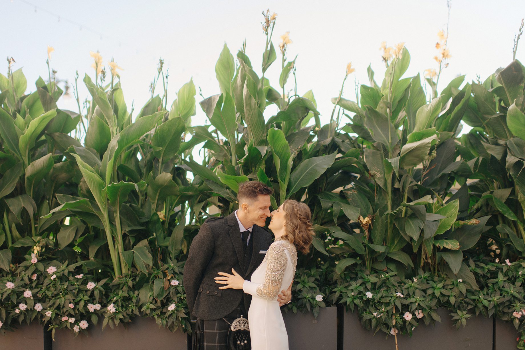 Romantic portrait of the couple in front of a lush green wall of tropical plants on their wedding day in an elevated editorial wedding photography in Detroit