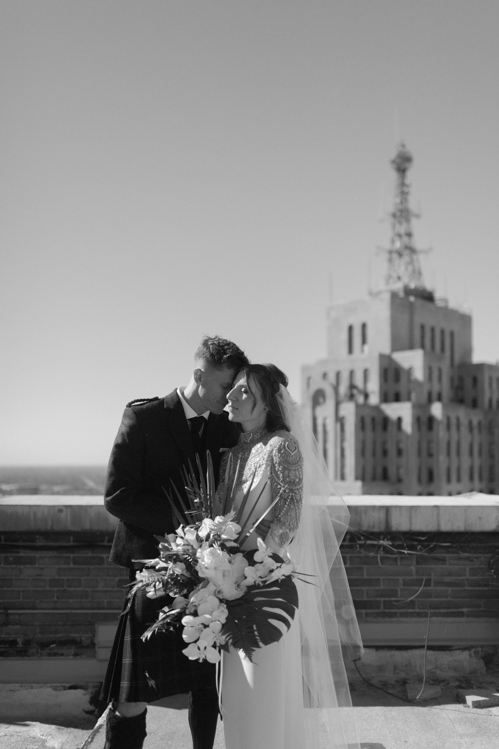 Bride and groom embrace on the guardian building rooftop with the historic David Stott Building behind them in a luxury editorial wedding portrait by Detroit wedding photographer Heather Jowett