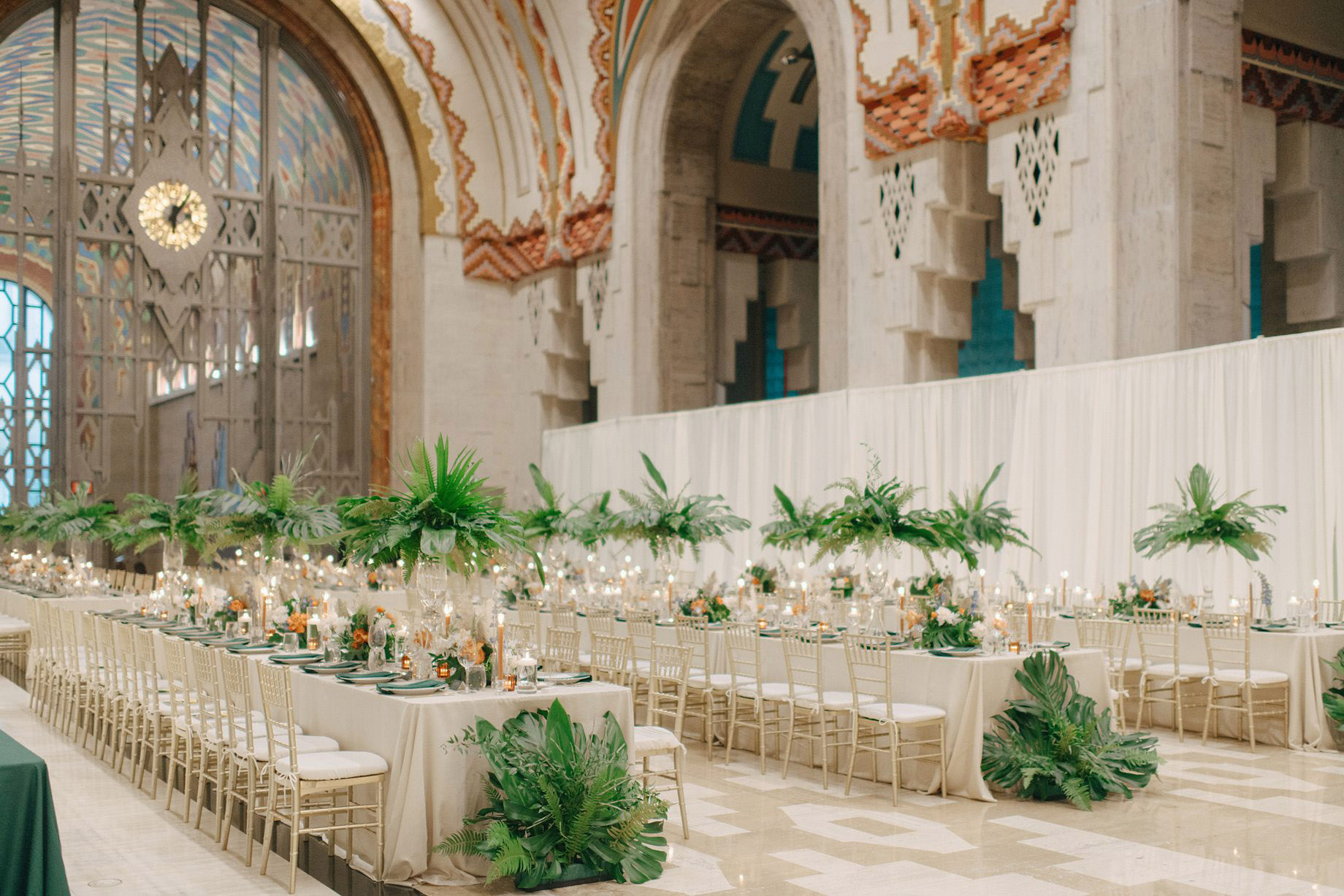 Elegant wedding reception setup by Simply Brilliant Events at the Guardian Building in Detroit featuring long tables with tropical greenery centerpieces