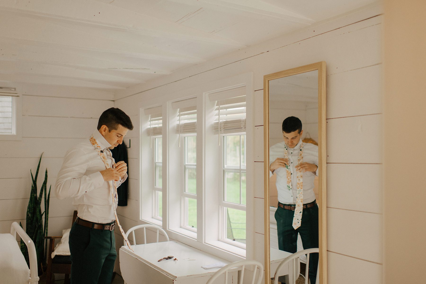 Groom adjusts floral tie in whitewashed room