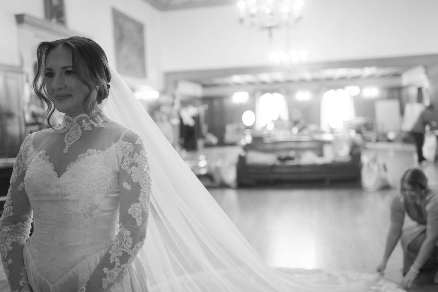 Bride beaming as her cathedral veil is fluffed by her bridesmaids