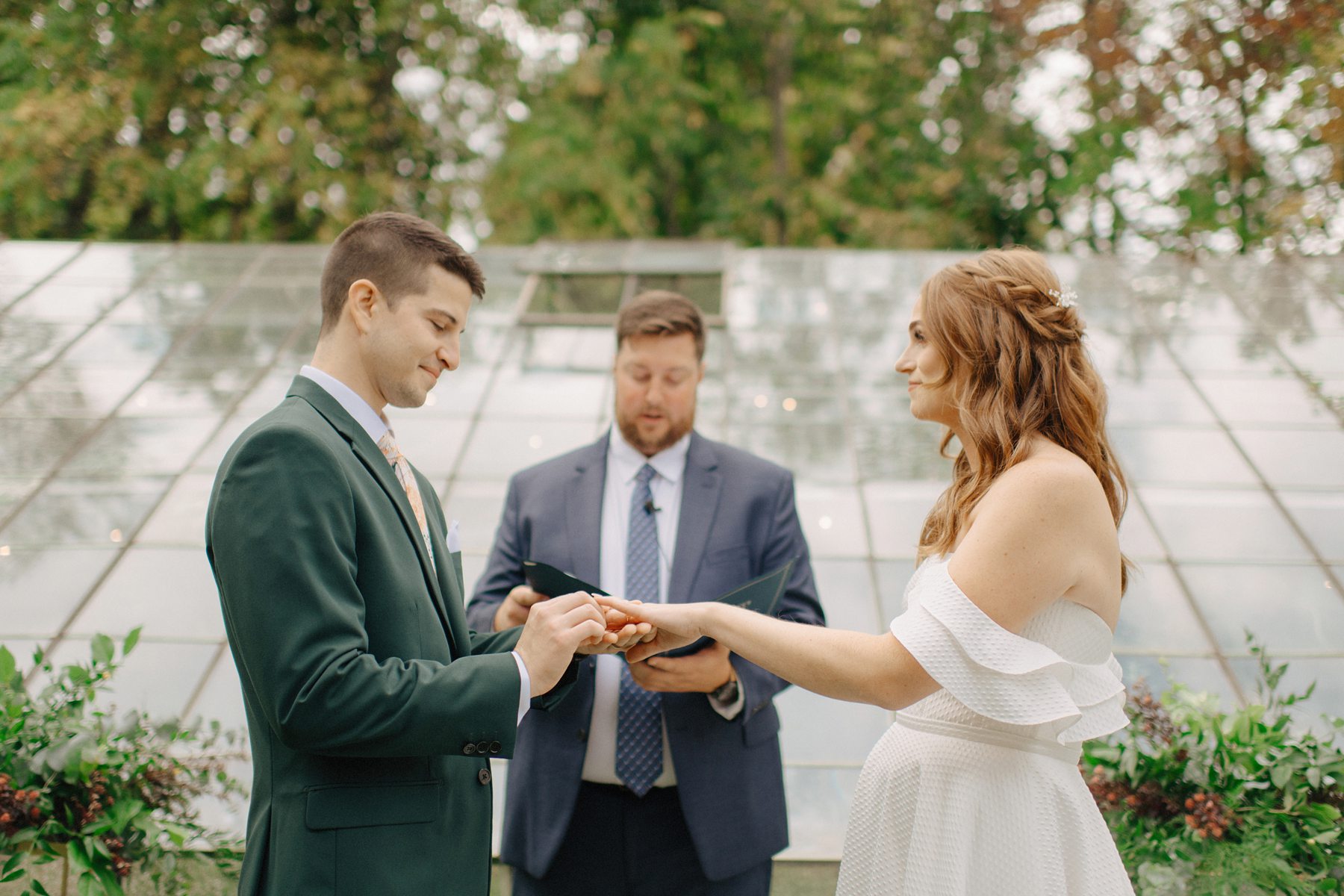 Groom places ring on brides finger during outdoor ceremony at Glass House Community