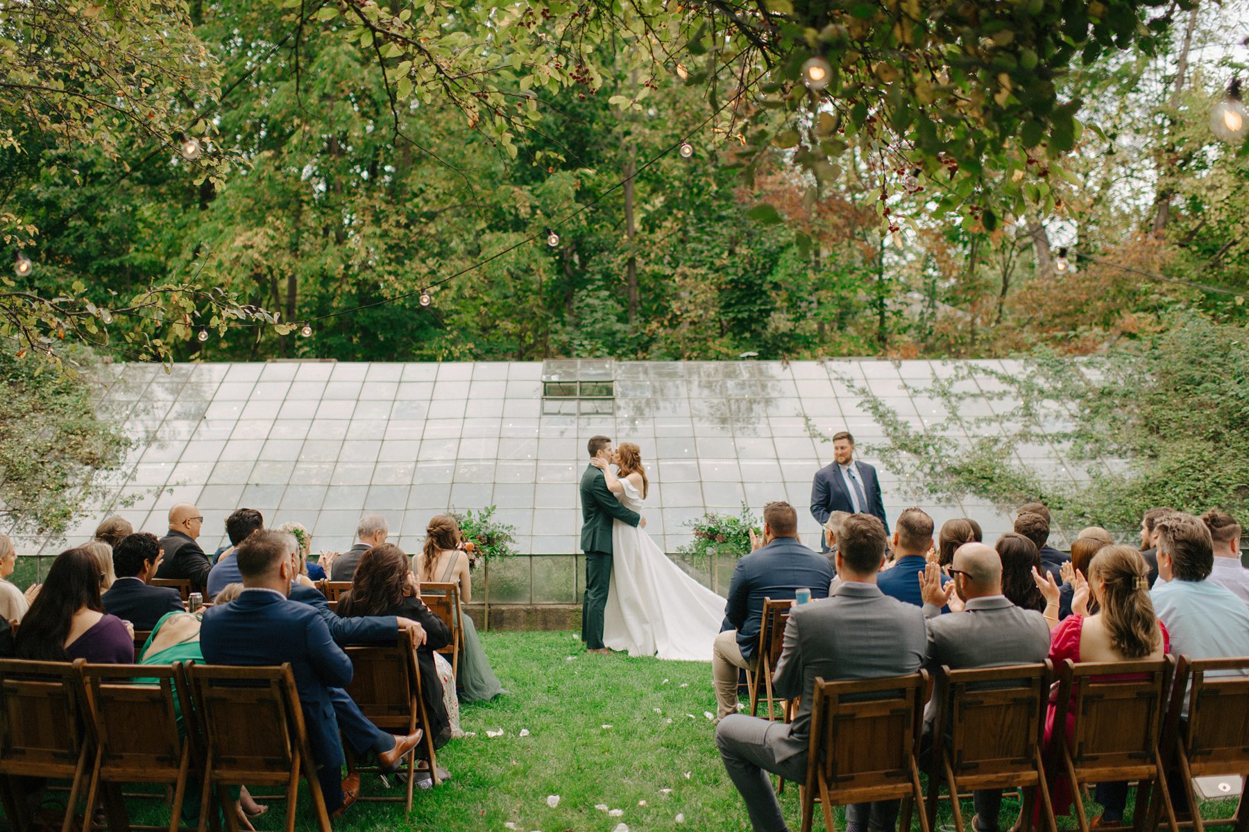 couple exchanges their first kiss as bride and groom in front of the greenhouse
