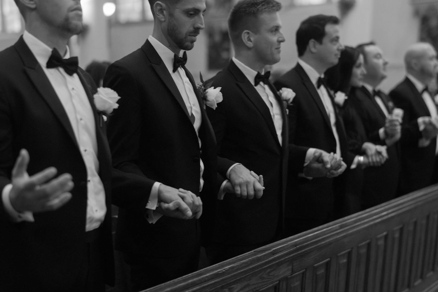 Guests standing in prayerful stillness during the Catholic wedding ceremony at Saints Peter and Paul Jesuit Church