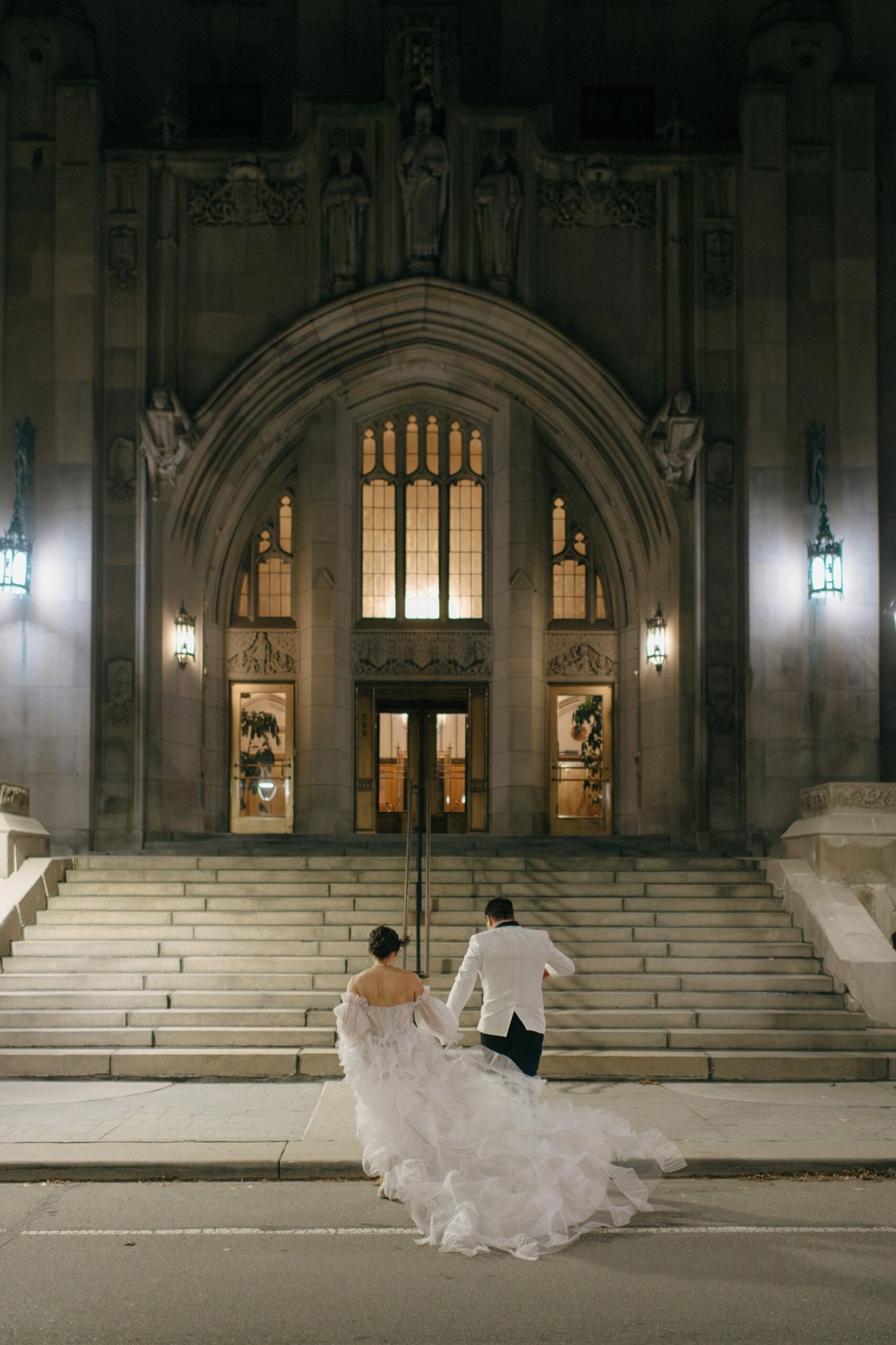 Bride and groom walking up the grand steps to their Detroit Masonic Temple wedding by Fine Art Wedding Photographer Heather Jowett