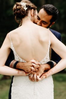 bride with henna on her hands being hugged by groom