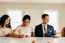 bride signs license while groom checks out his ring